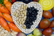 Dry beans are artfully arranged in the shape of a heart surrounded by vegetables
