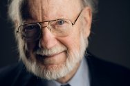 Headshot of William Campbell wearing glasses, a suit, and a tie with colorful insects on it.